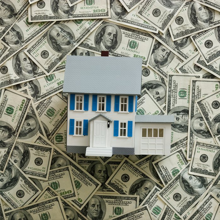 A model house resting on a pile of hundred-dollar bills